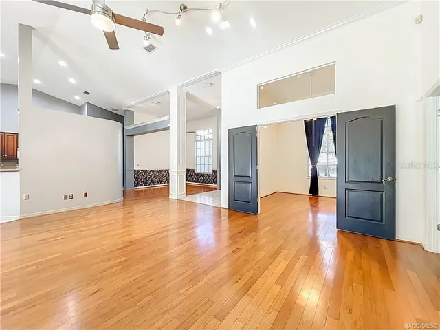 a view of an empty room with wooden floor and a ceiling fan