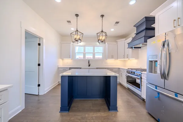 a kitchen with stainless steel appliances a sink dishwasher a stove a refrigerator and a dining table with wooden floor