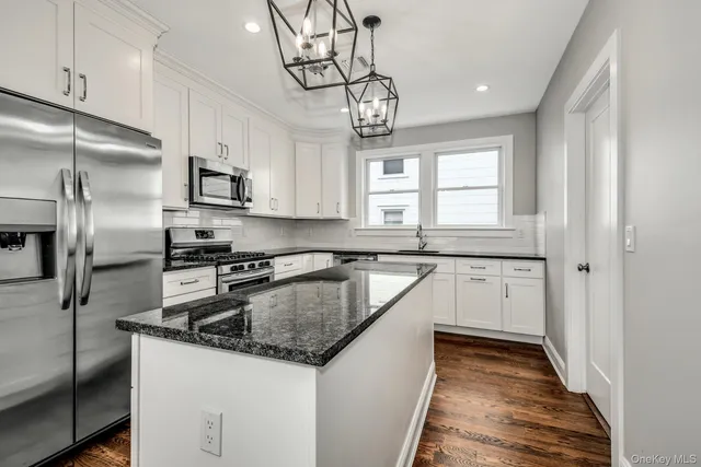 a kitchen with stainless steel appliances granite countertop a sink a stove a refrigerator cabinets and a window