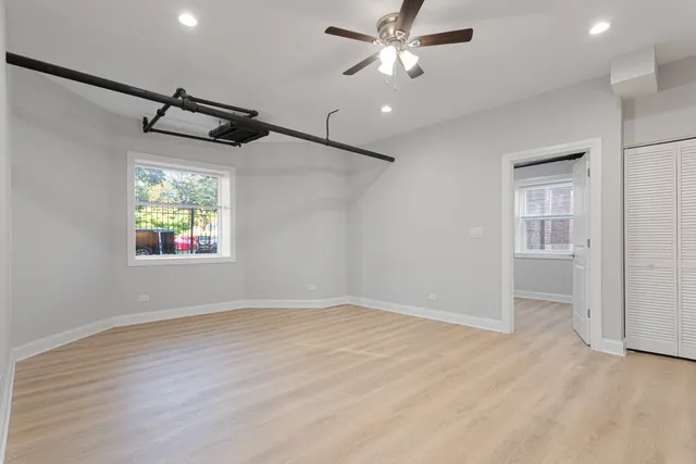 an empty room with wooden floor ceiling fan and windows