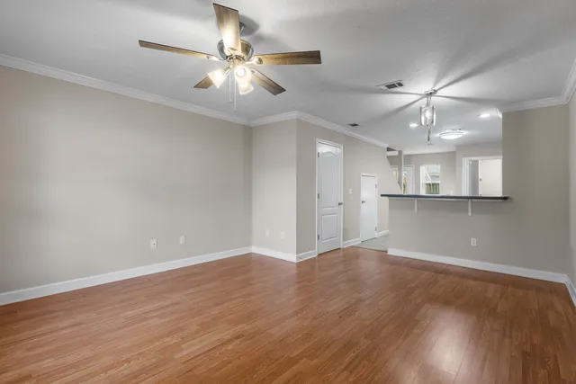 a view of an empty room with wooden floor and a ceiling fan