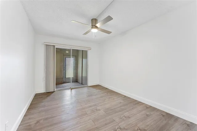 an empty room with wooden floor a ceiling fan and windows
