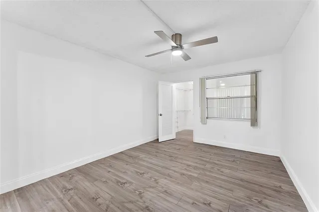 an empty room with wooden floor fan and windows
