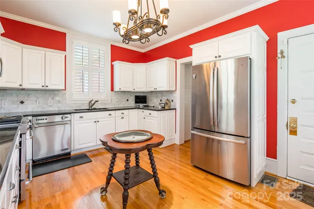 a kitchen with stainless steel appliances granite countertop a refrigerator a sink dishwasher a stove and white cabinets with wooden floor