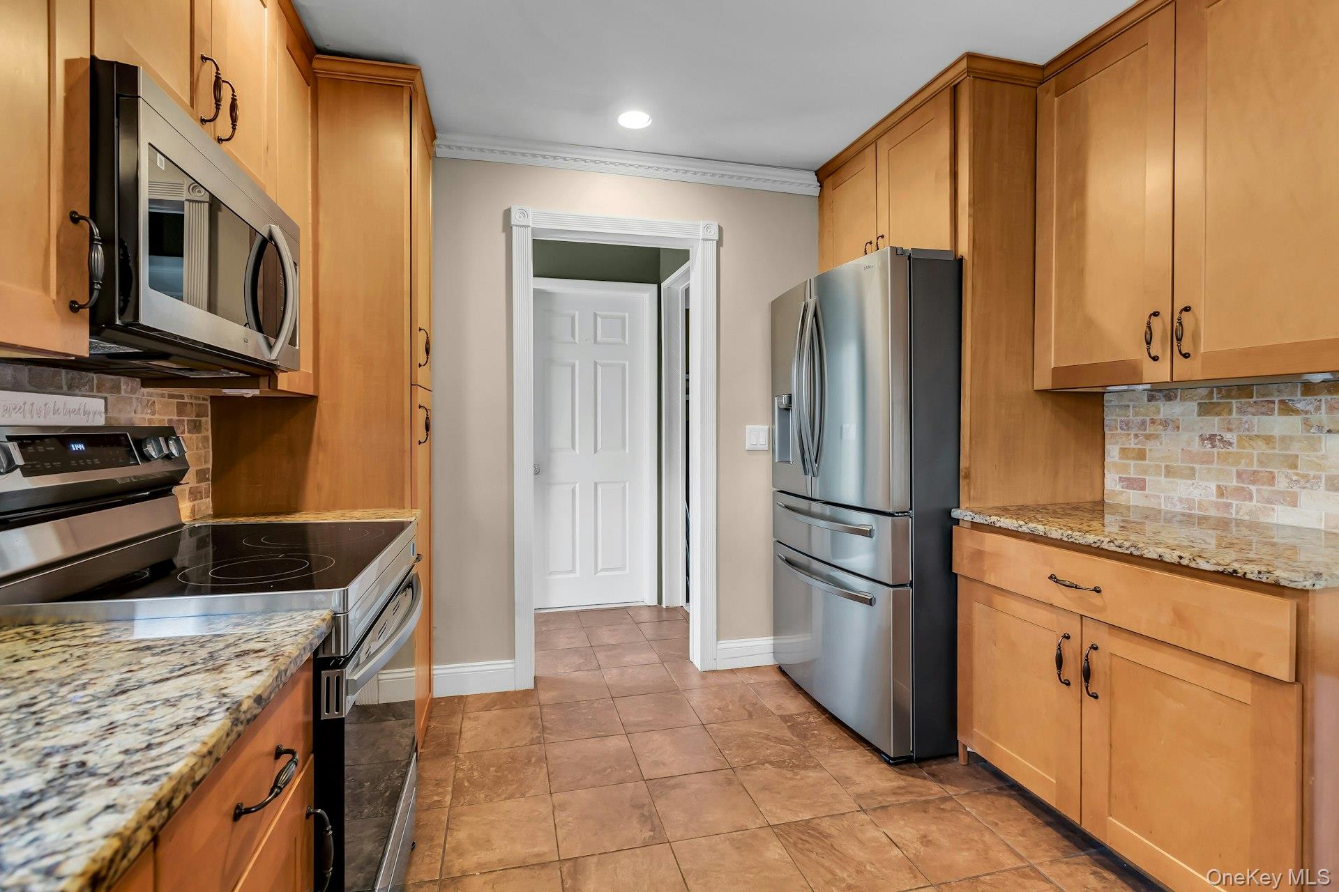 358 Rider Avenue Patchogue, NY 11772 - Photo 11 of 25 Kitchen with tasteful backsplash, stainless steel appliances, light stone countertops, light tile patterned floors, and crown molding