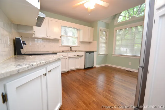 a kitchen with granite countertop a stove a sink and white cabinets with wooden floor