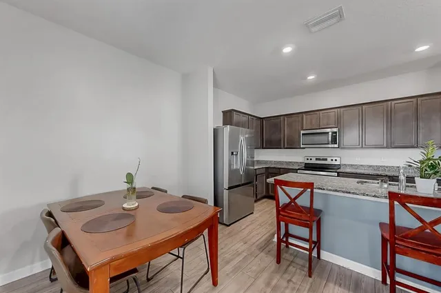 a kitchen with stainless steel appliances a sink a stove a refrigerator dining table and chairs