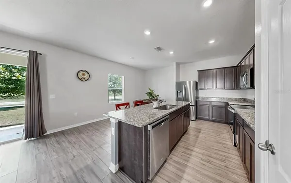 a kitchen with stainless steel appliances granite countertop a stove top oven a sink dishwasher a refrigerator and a oven with wooden floor