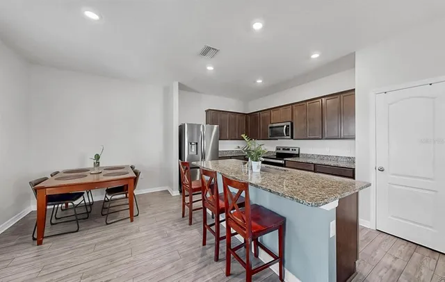 a kitchen with stainless steel appliances granite countertop a table chairs sink and cabinets
