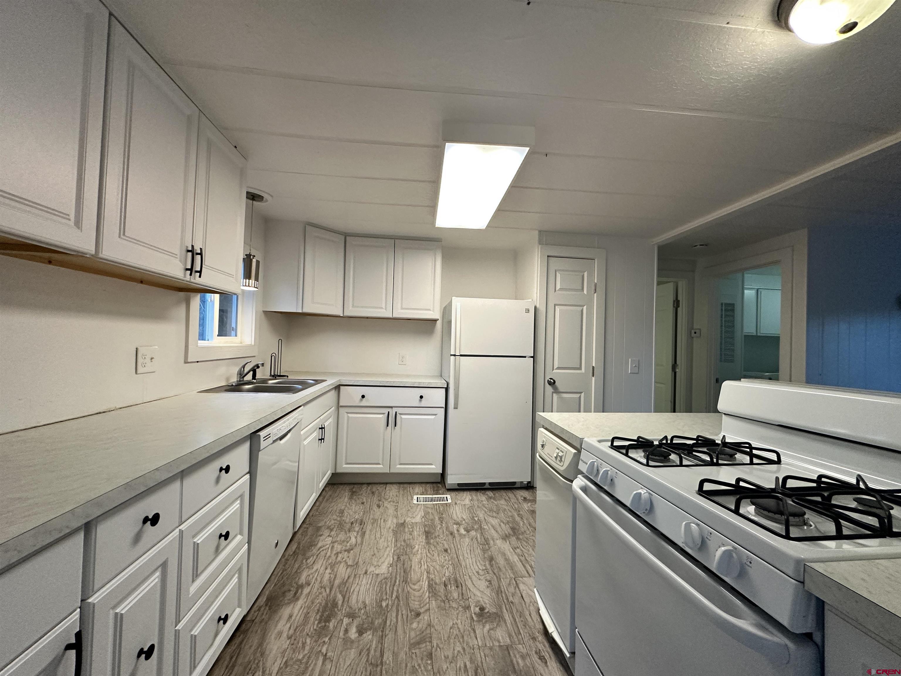 468 Rio Grande Road South Fork, CO 81154 - Photo 10 of 43 a kitchen with stainless steel appliances a white stove top oven a sink dishwasher and white cabinets with wooden floor