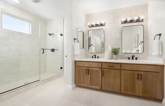 a spacious bathroom with double vanity a mirror and a shower