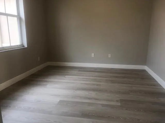 a view of an empty room with wooden floor and a window