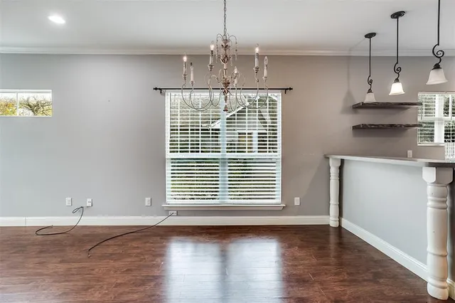 a view of an empty room with wooden floor kitchen view and a window