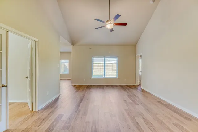 an empty room with wooden floor fan and windows