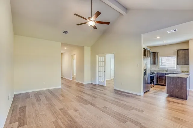 a view of an empty room and kitchen with wooden floor