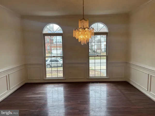 an empty room with wooden floor chandelier and windows
