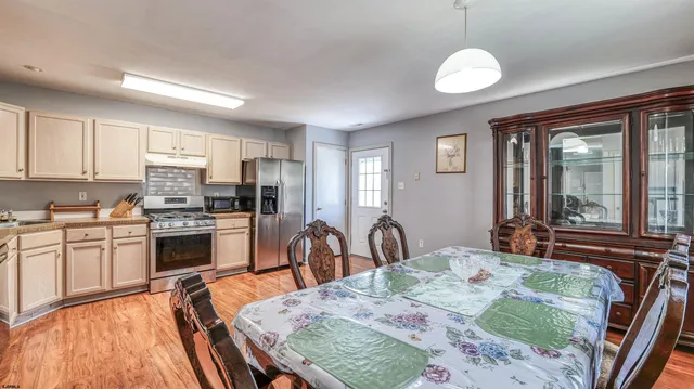 a kitchen with stainless steel appliances granite countertop a stove top oven a sink a dining table and chairs with wooden floor