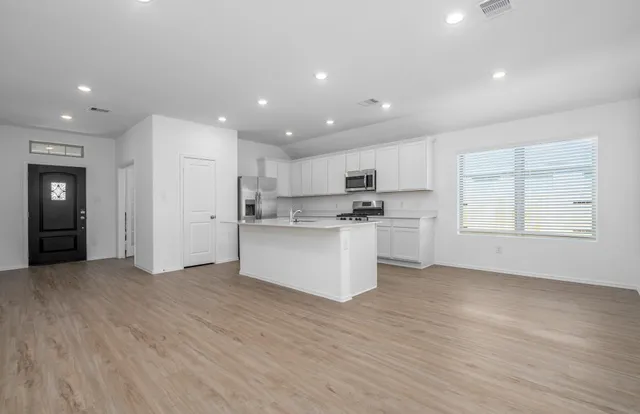 a view of kitchen with granite countertop refrigerator oven sink and white cabinets with wooden floor