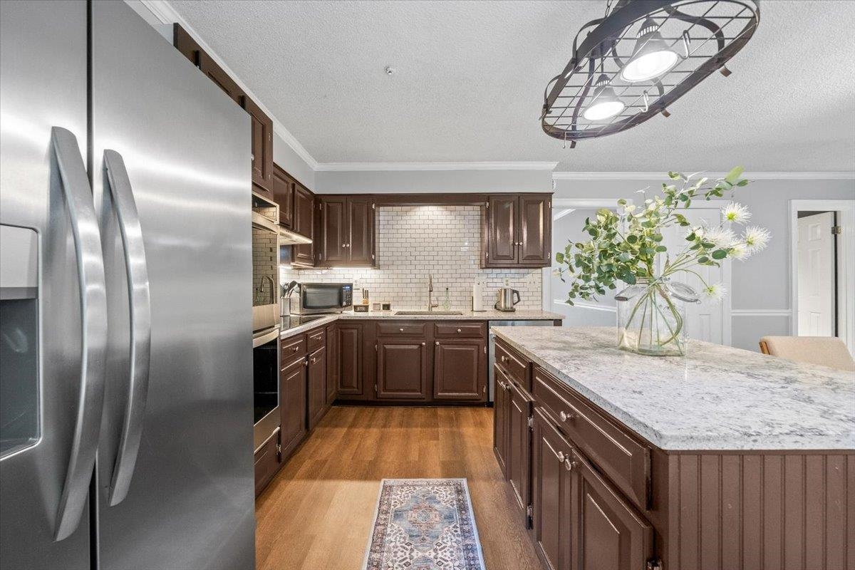 8162 Walnut Creek Road Memphis, TN 38018 - Photo 14 of 33 Kitchen featuring appliances with stainless steel finishes, wood finished floors, crown molding, decorative backsplash, and a center island