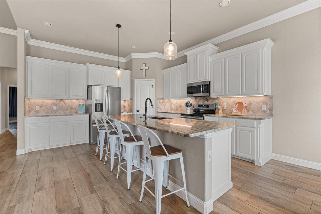 9708 Puma Trail Godley, TX 76044 - Photo 11 of 40 a kitchen with stainless steel appliances granite countertop a stove top oven a refrigerator a sink and a dining table with wooden floor