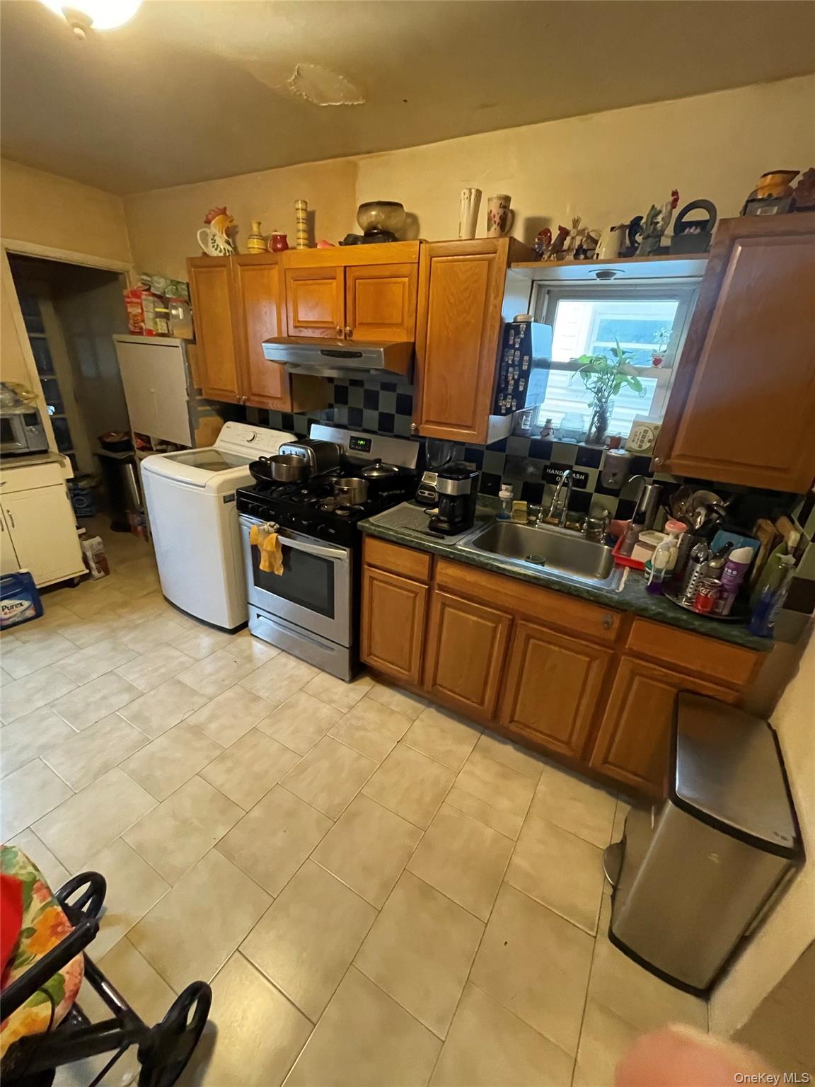 Kitchen with brown cabinets, stainless steel range with gas cooktop, washer / clothes dryer, under cabinet range hood, and dark stone countertops