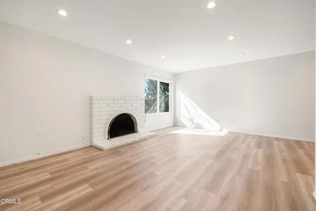 a view of an empty room with wooden floor fireplace and a window