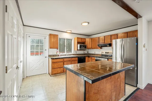 a kitchen with stainless steel appliances kitchen island granite countertop a refrigerator a stove and white cabinets with wooden floor