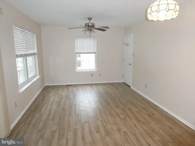 an empty room with wooden floor fan and windows