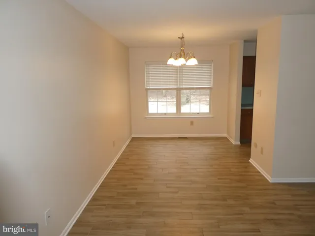 an empty room with wooden floor chandeliers and kitchen view