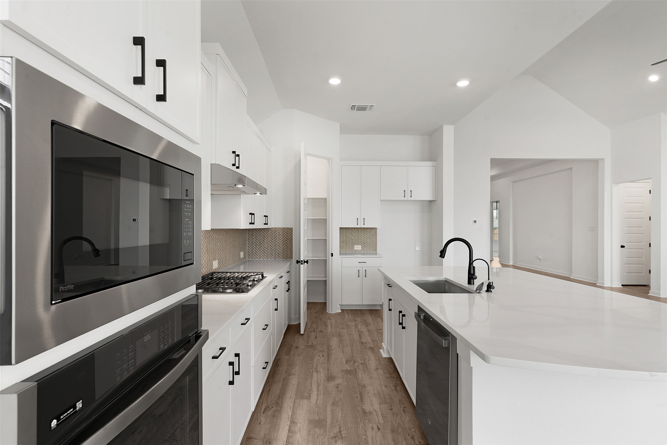 19504 Domino Champ Road Pflugerville, TX 78660 - Photo 11 of 24 Kitchen featuring stainless steel appliances, a spacious island, white cabinetry, light wood-style floors, and light stone counters