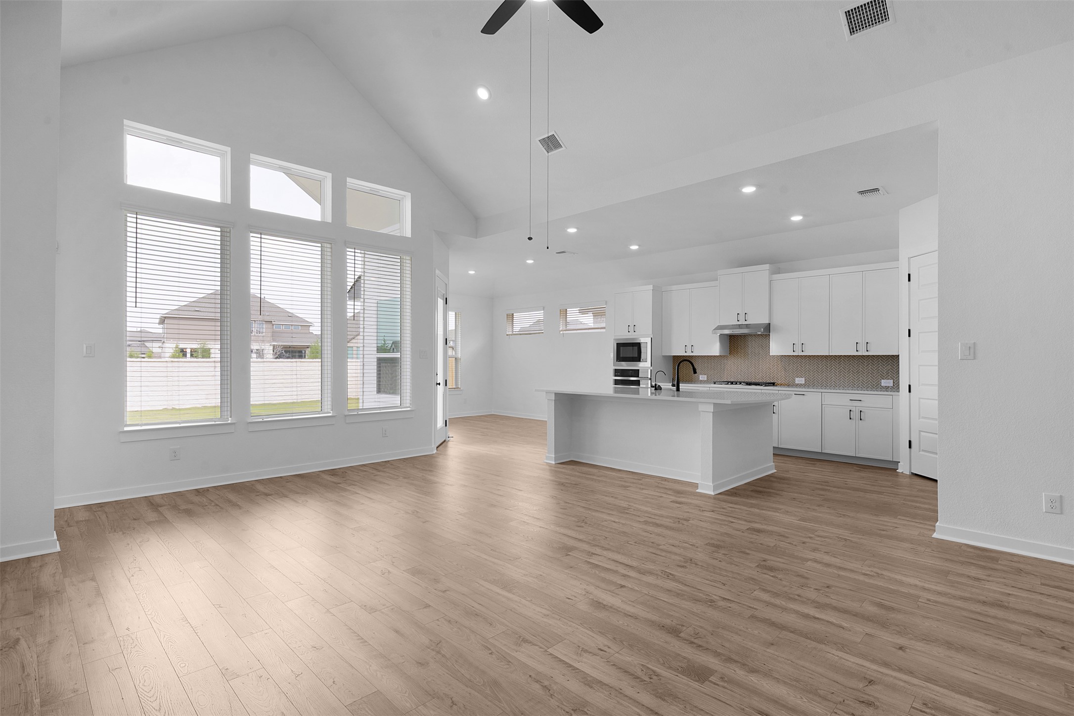 19504 Domino Champ Road Pflugerville, TX 78660 - Photo 9 of 24 Kitchen featuring white cabinetry, an island with sink, a ceiling fan, decorative backsplash, and light wood finished floors