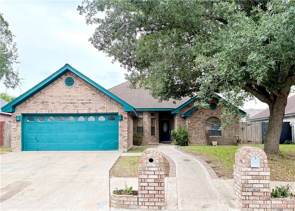 View of front facade with an attached garage, driveway, brick siding, and fence