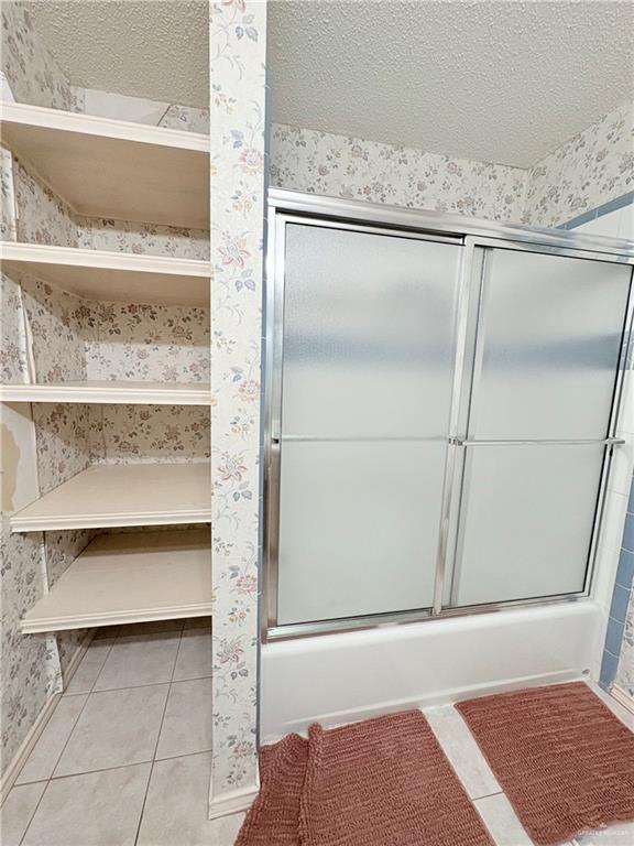 2218 Lawndale Road Mission, TX 78572 - Photo 21 of 24 Full bath with a textured ceiling, wallpapered walls, bath / shower combo with glass door, baseboards, and tile patterned flooring