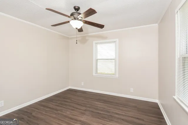 an empty room with wooden floor ceiling fan and windows