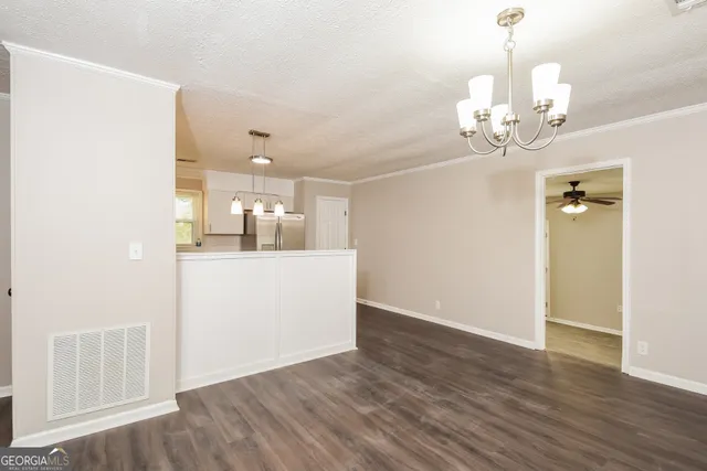a view of an empty room with kitchen and wooden floor