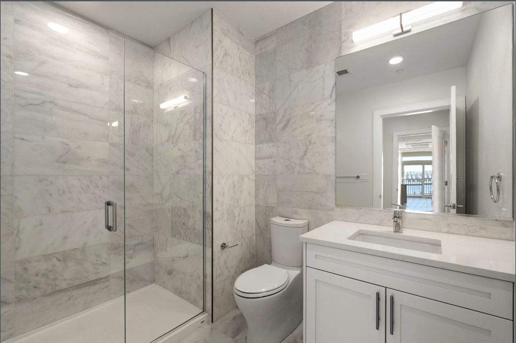 301 Border Street, Unit 610 Boston, MA 02128 - Photo 5 of 17 a bathroom with a granite countertop toilet a sink and shower
