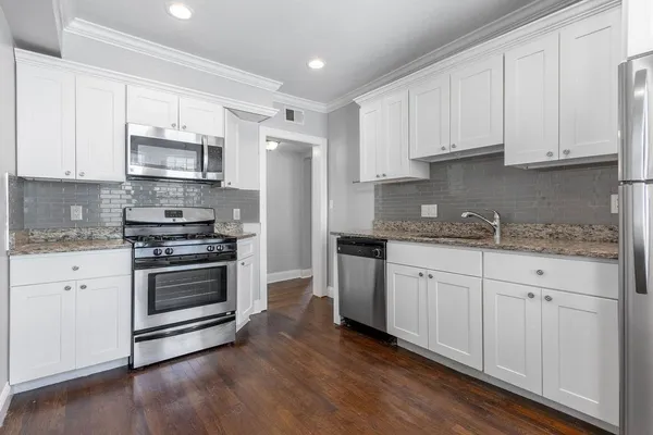 a kitchen with granite countertop white cabinets stainless steel appliances and wooden floor