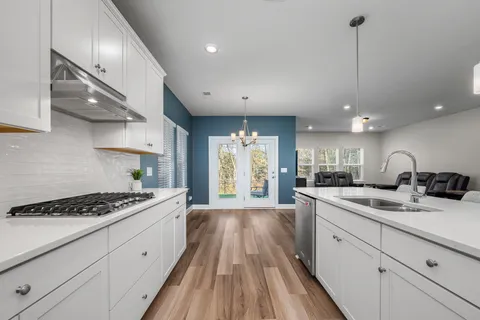 a kitchen with stainless steel appliances kitchen island granite countertop a stove a sink dishwasher and white cabinets with wooden floor