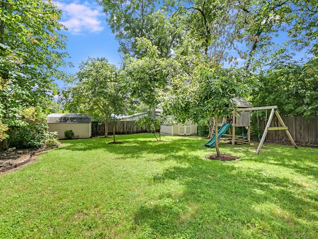 a view of a backyard with a slide trees and wooden fence