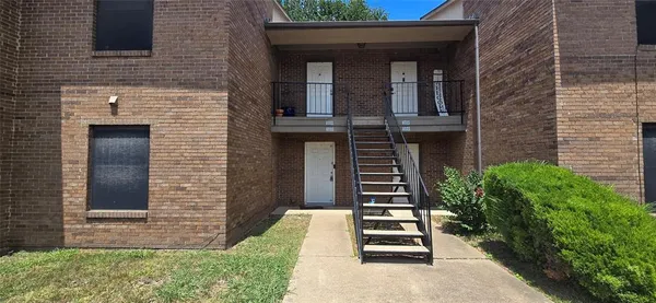 a view of a brick house with plants and wooden fence