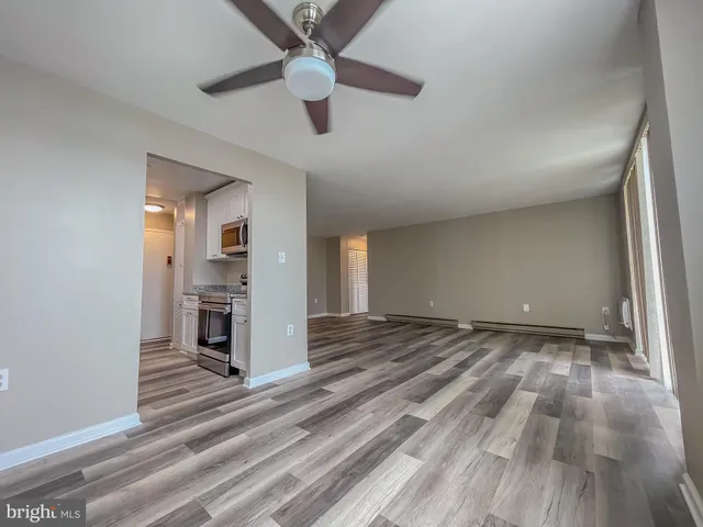 an empty room with wooden floor a ceiling fan and kitchen view