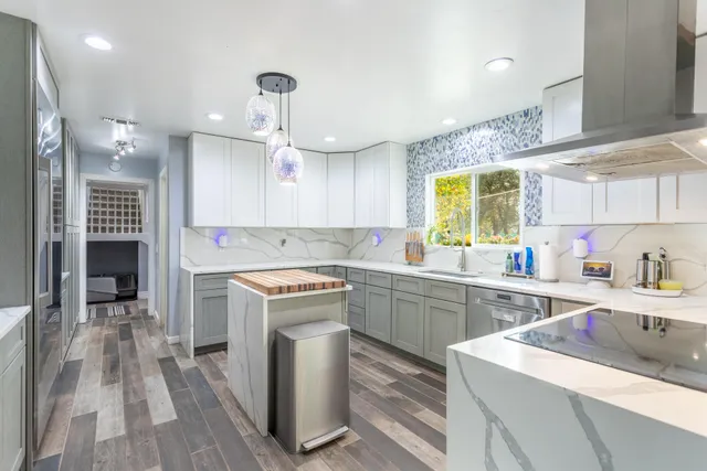 a kitchen with stainless steel appliances granite countertop a stove a refrigerator a sink and a dining table with wooden floor