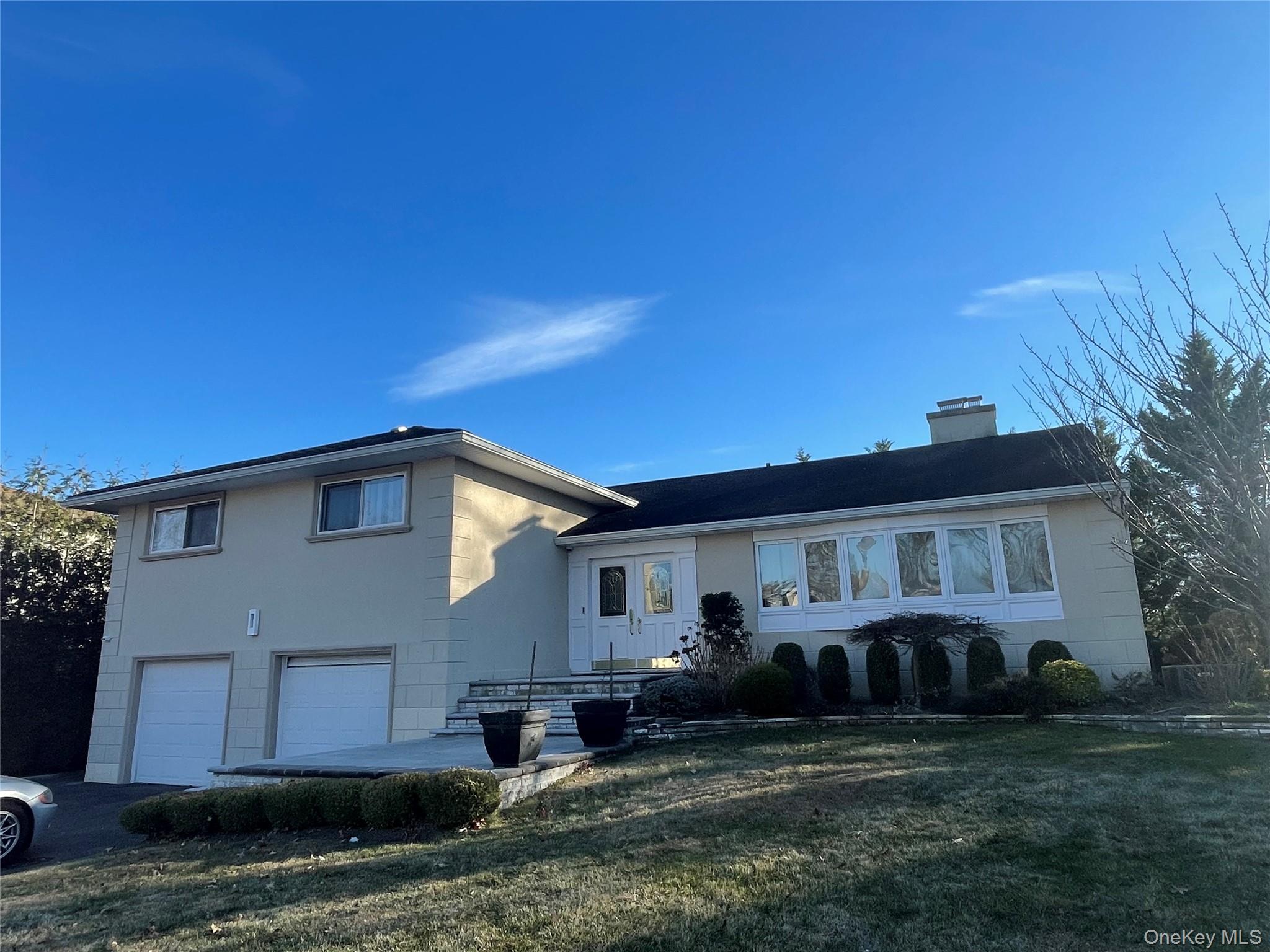 Tri-level home featuring a garage, a chimney, a front lawn, and driveway