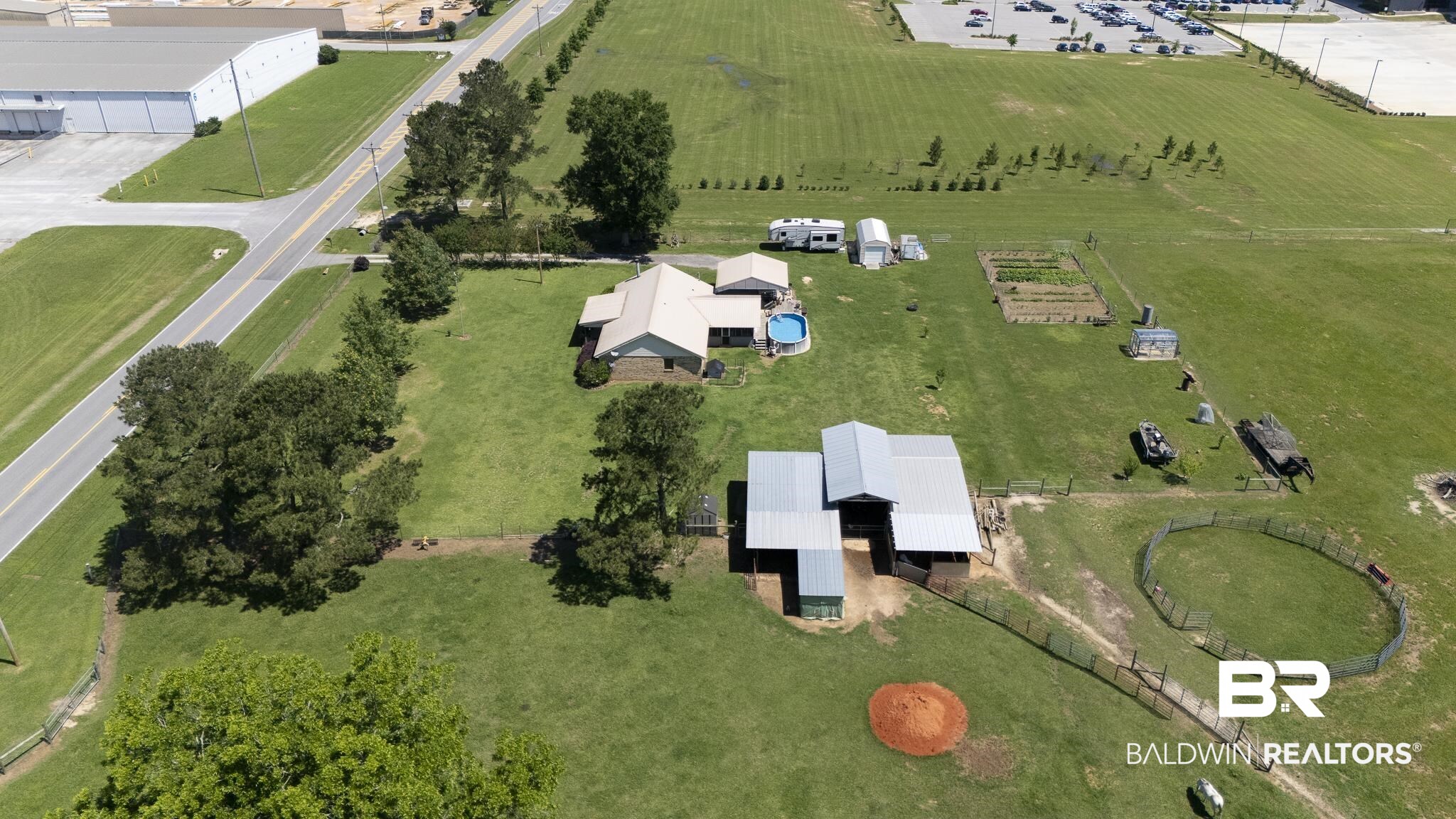 30580 County Road 49 Loxley, AL 36551 - Photo 21 of 32 Expansive property featuring a main residence with a gabled roof, an auxiliary structure with a metal roof, an above-ground pool, fenced garden plots, and a circular fenced area