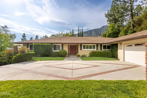 a view of house in front of a big yard with large trees