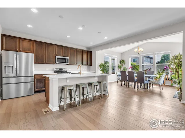 a kitchen with stainless steel appliances granite countertop a refrigerator a stove a sink a dining table and chairs with wooden floor