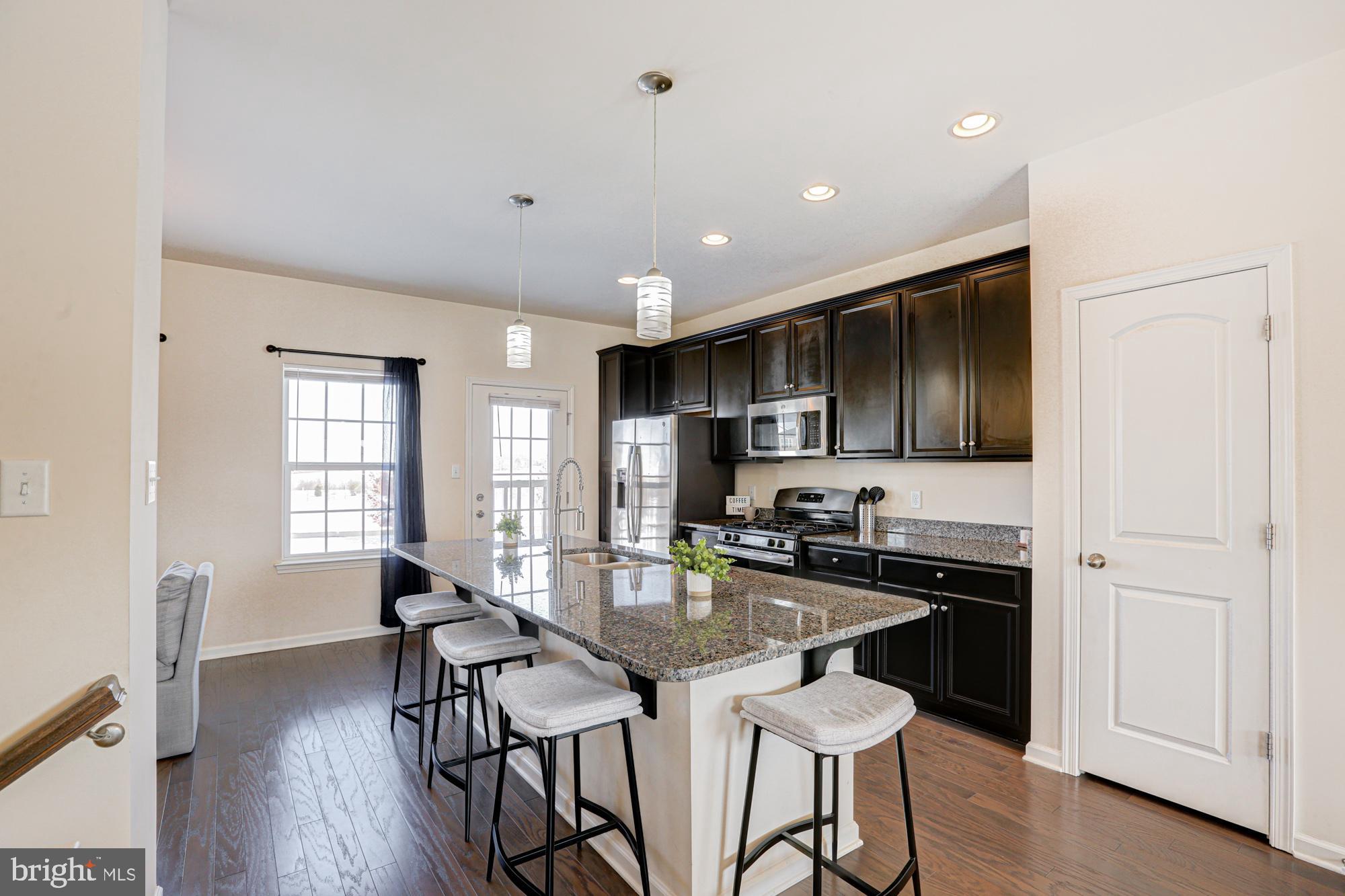 1102 Wickersham Way Middletown, DE 19709 - Photo 27 of 68 a kitchen with stainless steel appliances kitchen island granite countertop a stove a refrigerator a sink a dining table and chairs with wooden floor