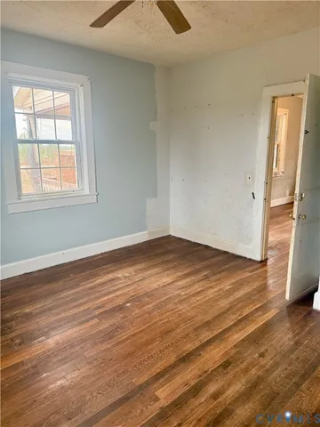 an empty room with wooden floor chandelier fan and windows