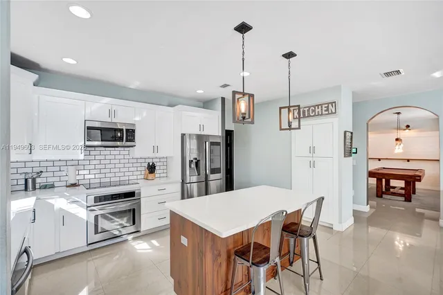 a kitchen with stainless steel appliances kitchen island granite countertop a refrigerator a stove top oven a sink a dining table and chairs with wooden floor