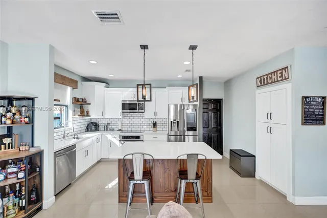 a kitchen with stainless steel appliances kitchen island granite countertop a dining table chairs and a refrigerator